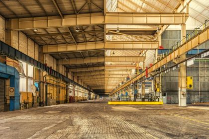 Interior amplo de um armazém industrial com estruturas metálicas, teto alto e espaço para operações.