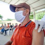 Morador recebe uma vacina de um profissional de saúde em atendimento realizado ao ar livre.