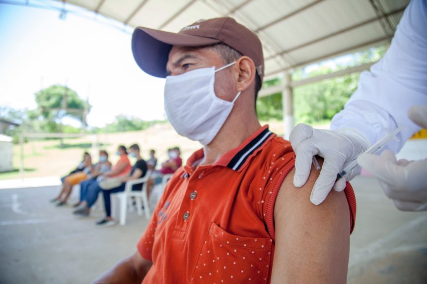 Morador recebe uma vacina de um profissional de saúde em atendimento realizado ao ar livre.