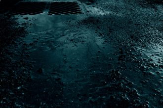 Água da chuva acumulada junto ao meio-fio e à drenagem de uma rua pavimentada.