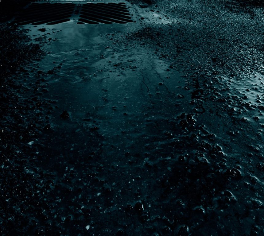Água da chuva acumulada junto ao meio-fio e à drenagem de uma rua pavimentada.