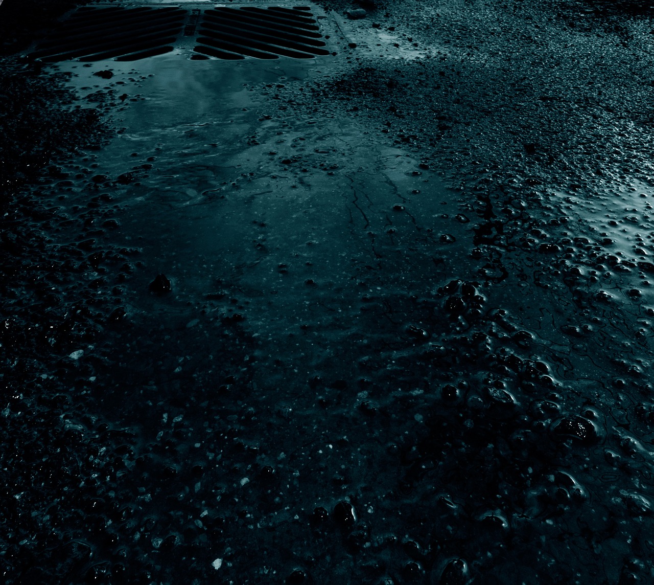 Água da chuva acumulada junto ao meio-fio e à drenagem de uma rua pavimentada.